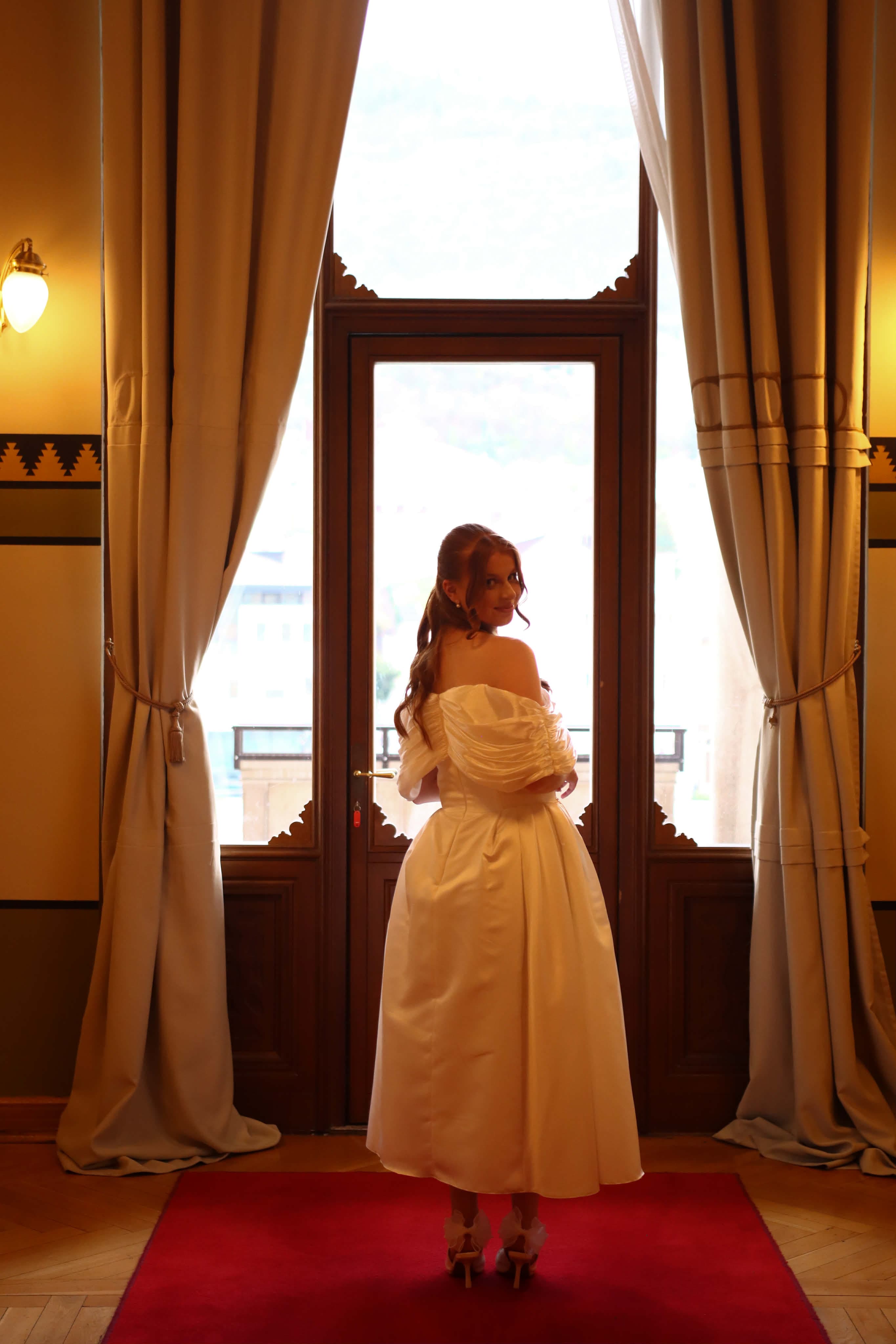 The back of Ena's custom off-shoulder gown by the window, made to her measurements