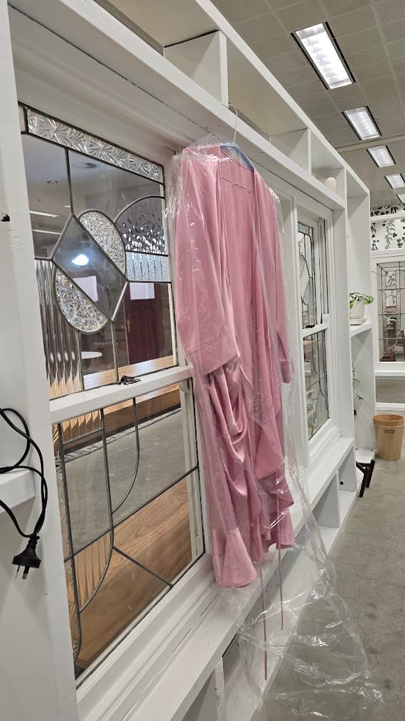 A finished dusty-pink satin dress in a garment bag hanging on a white frame in the Spacecubed coworking space