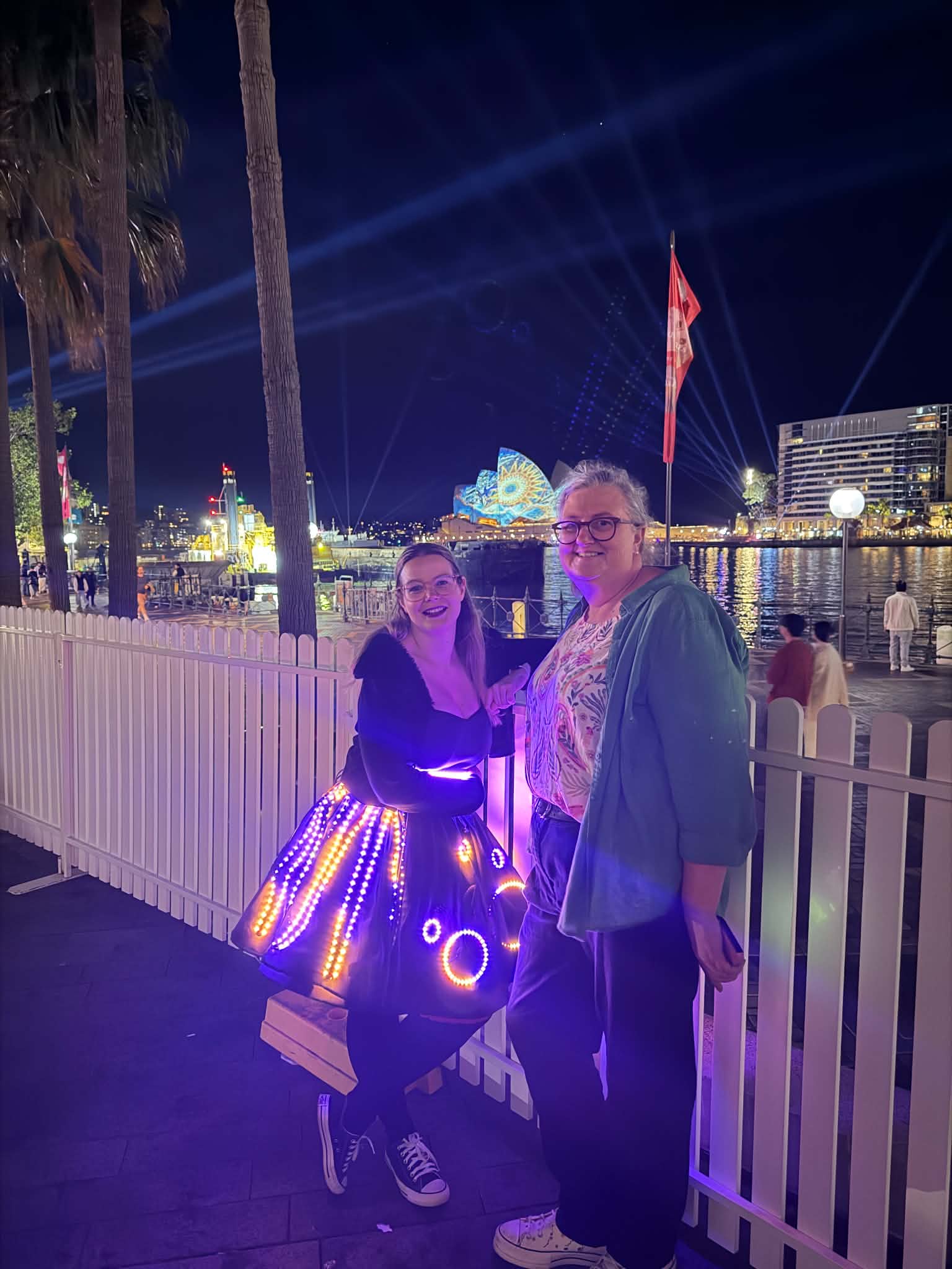 Kate in the lit dress on Sydney Harbour at night, the Opera House lit up behind her