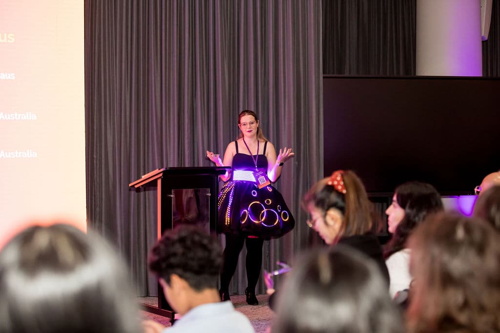 Kate speaking at a lectern in the lit dress, seen over the heads of the audience