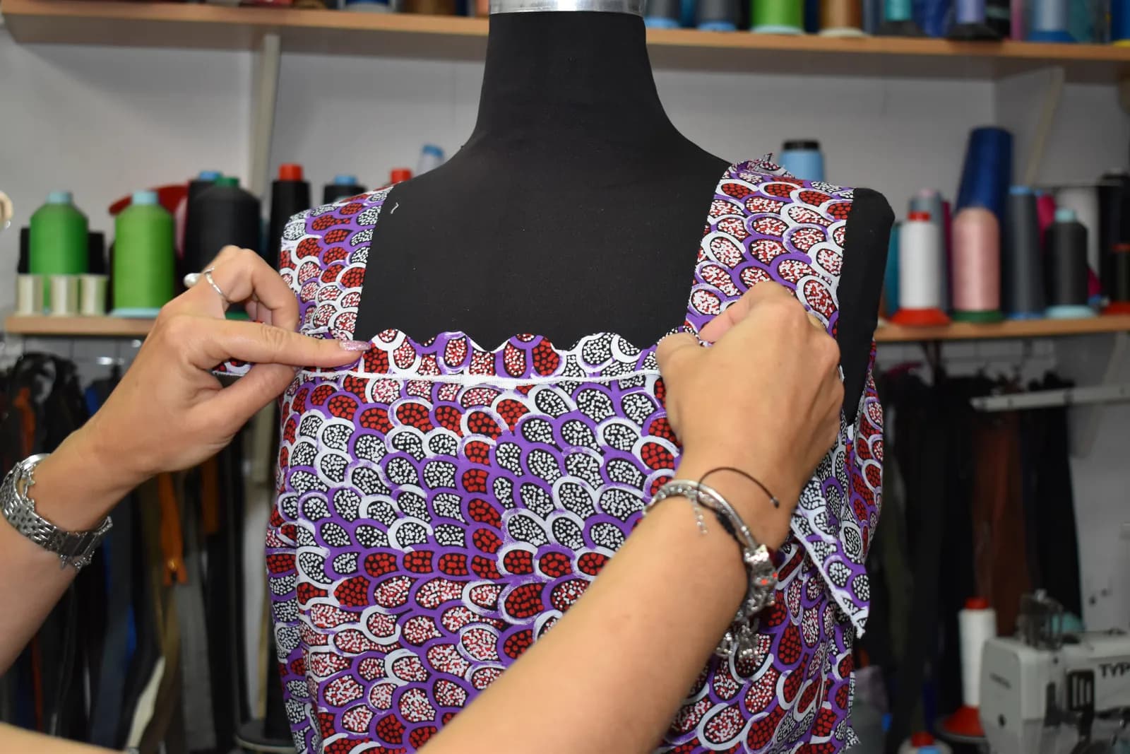 Enisa’s hands adjusting the square neckline of the print dress on the form