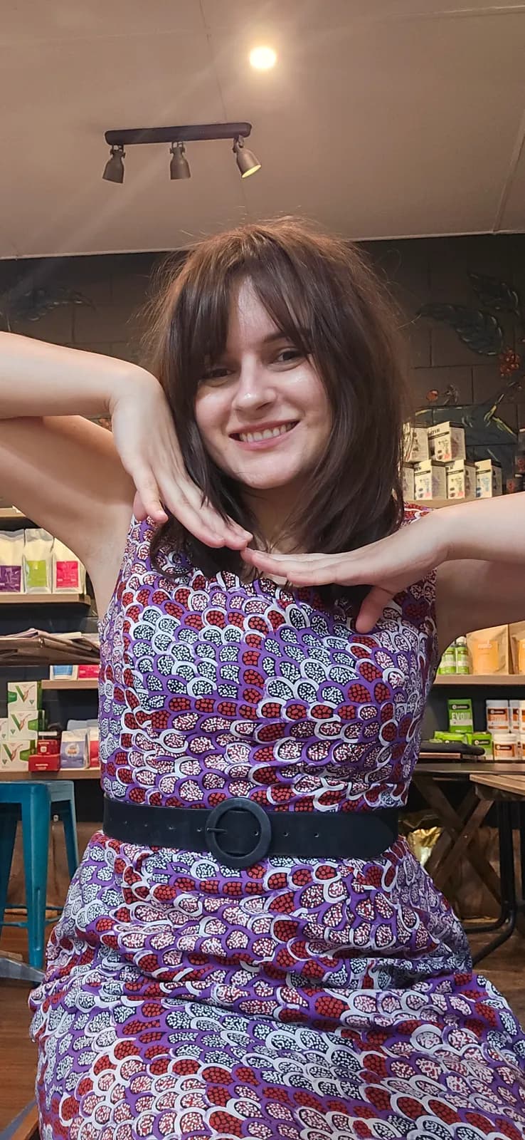 A woman smiling in the finished purple print dress with a black belt