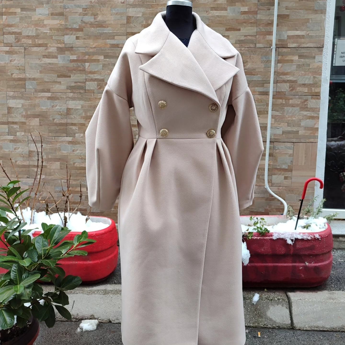 A custom double-breasted coat in cream twill on a mannequin — sleeve and body length made to the wearer's measurements