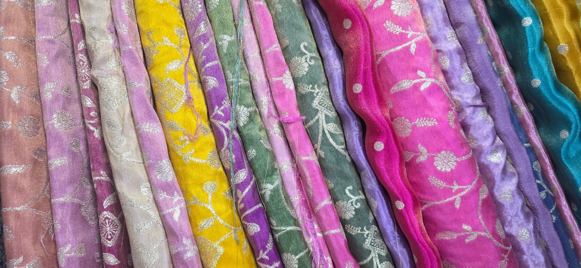 A rail of embroidered silks in pinks, purples, greens, gold and teal, sourced near the tailor