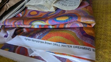 A bolt of Water Dreaming fabric with the artist's name, Agnes Nampijinpa Brown, printed on the selvedge