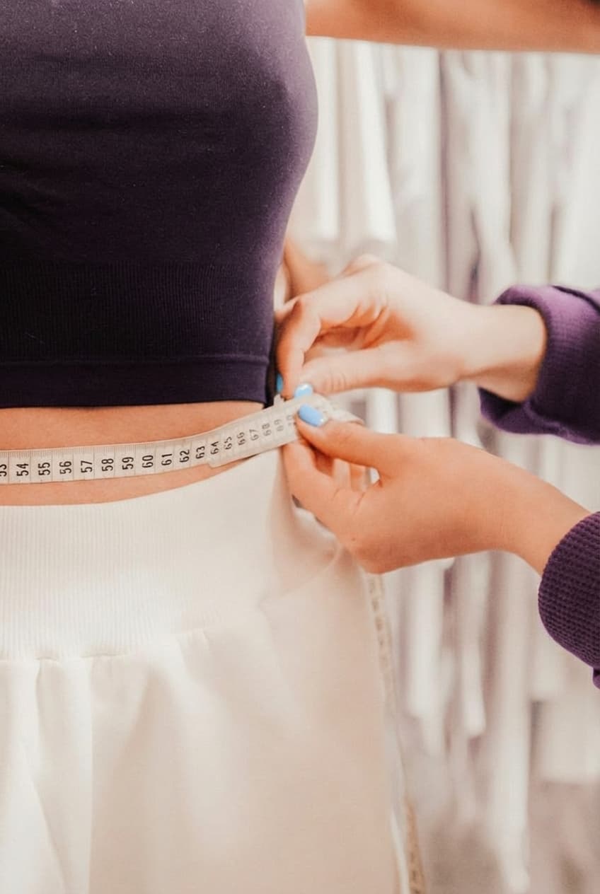 A tailor measuring a woman's waist with a soft measuring tape, taking the measurements for a custom made garment