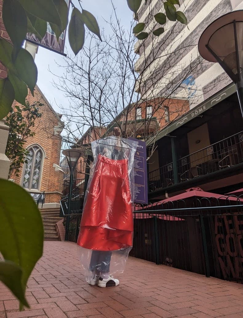 A red satin dress in a clear garment bag held up on a Perth laneway